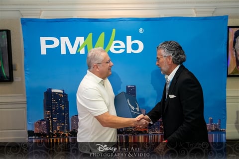 Zwei M�nner geben sich vor einem blauen Hintergrund mit dem PMWeb-Logo und einer Skyline die Hand und feiern einen Erfolg.