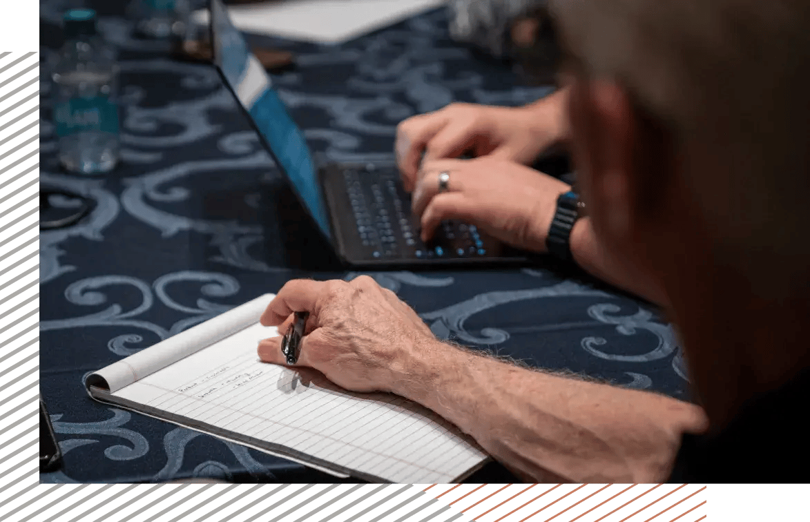 Close-up of people taking notes and typing on a laptop during a meeting or workshop.