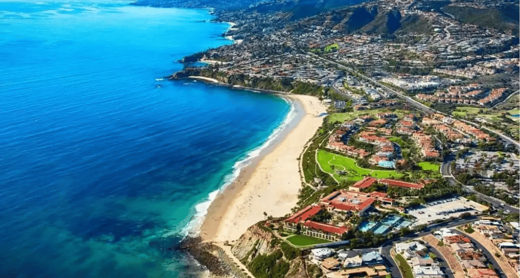 Aerial view of a beautiful coastline with sandy beaches, vibrant blue waters, and residential areas nestled between mountains and the sea.