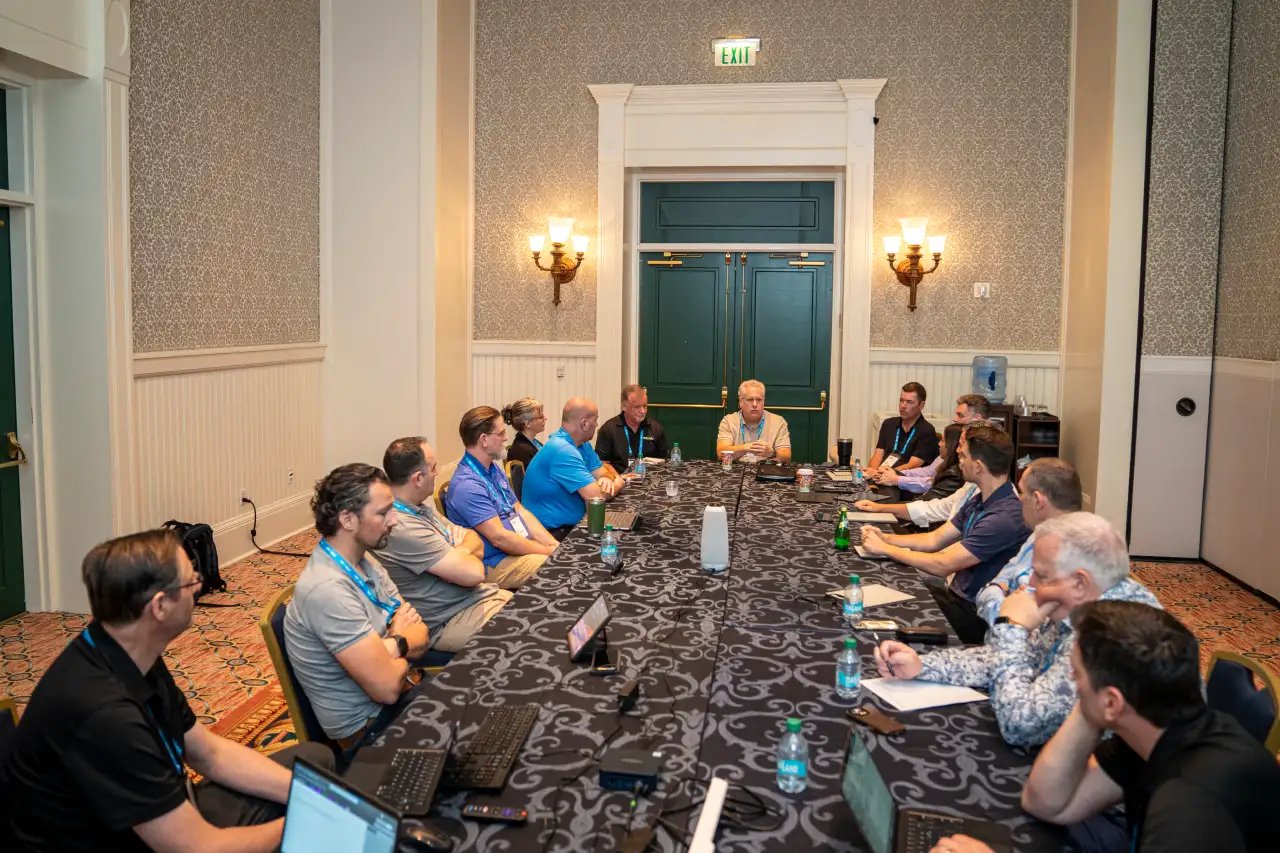 Group of professionals in a conference room having a meeting around a long table, representing PMWeb's collaboration with partners.