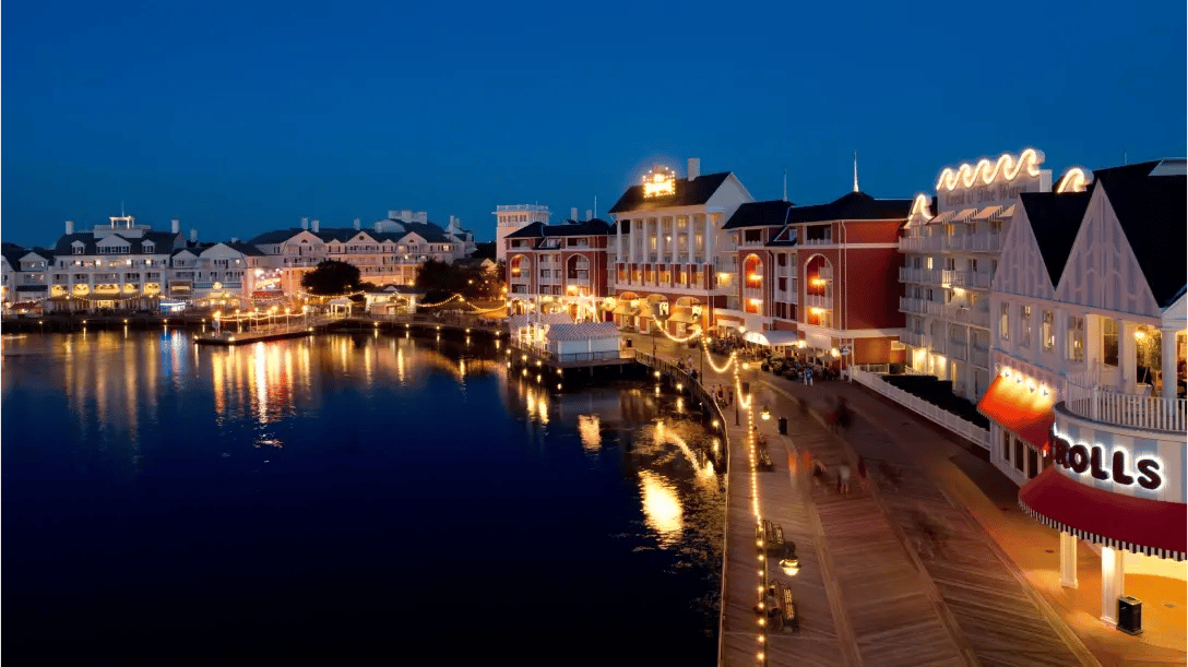 A picturesque waterfront scene at night featuring illuminated buildings and a serene lake reflecting the lights.